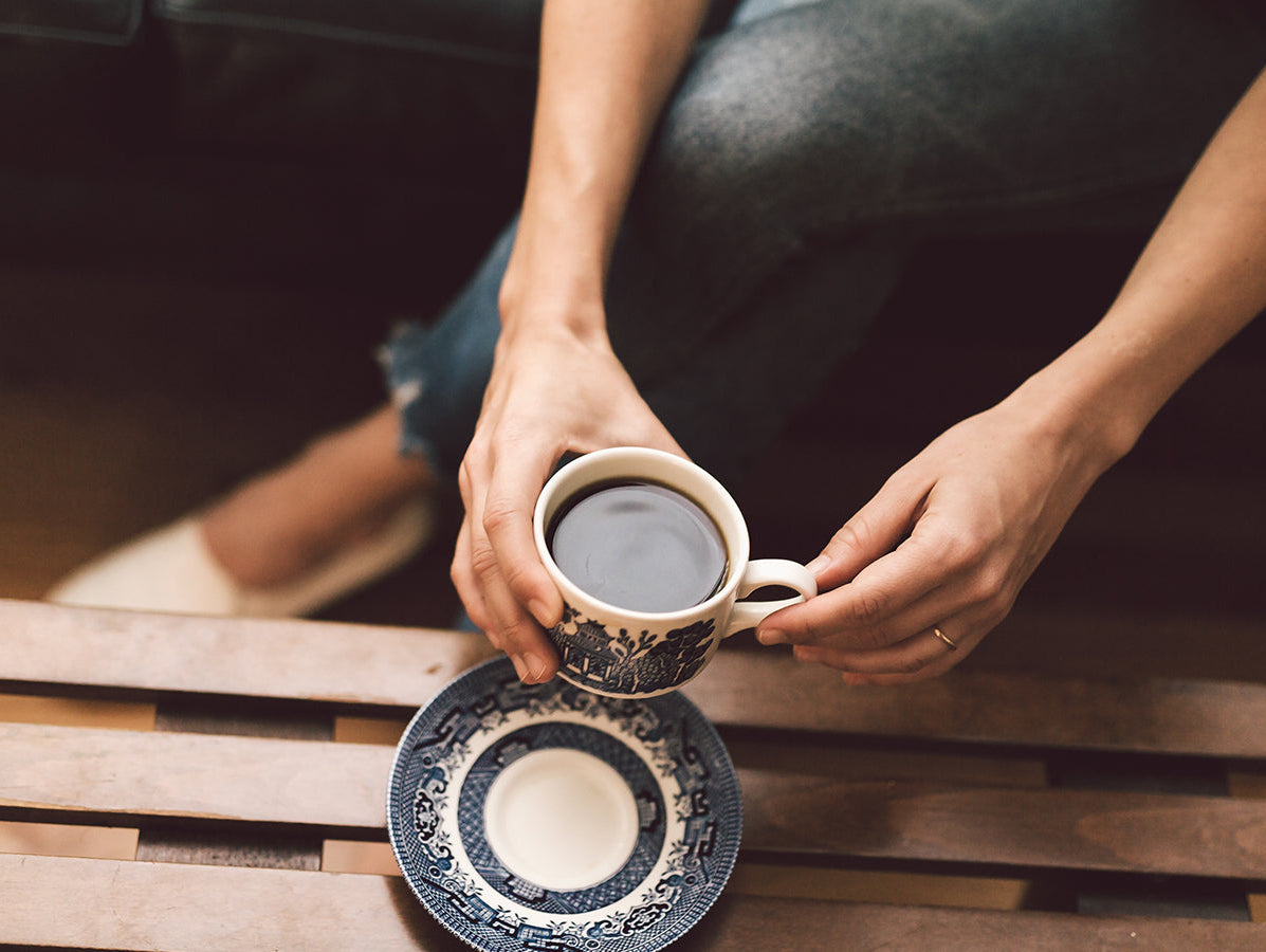 Person holding a cup of coffee over a table